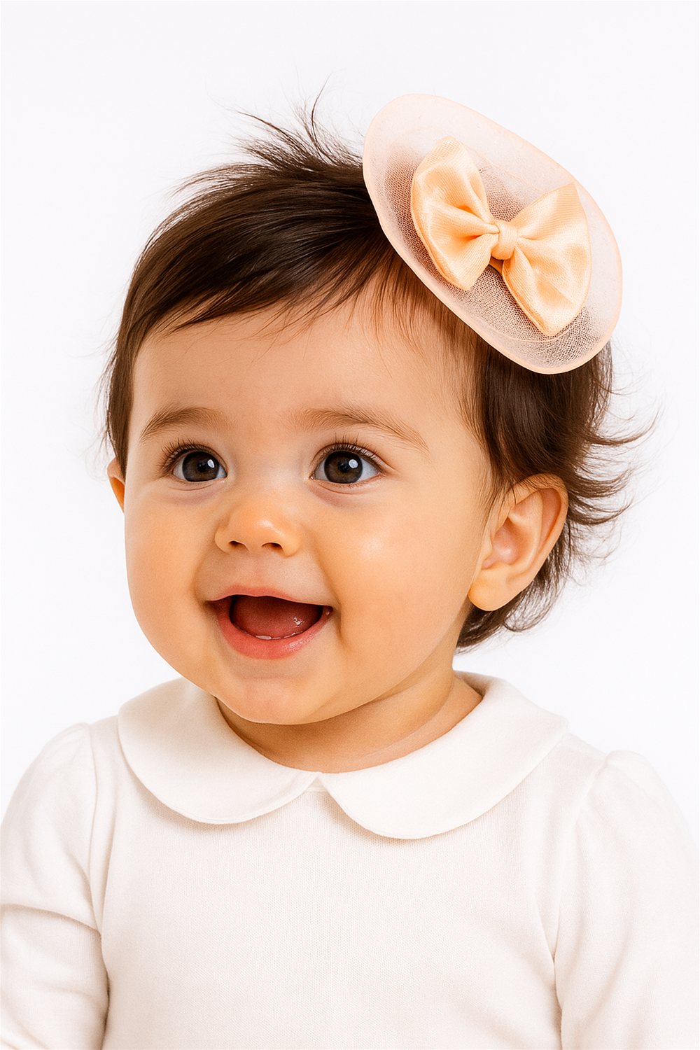 Smiling baby girl wearing peach bow hair clip on side of head, dressed in white outfit, looking adorable and happy.