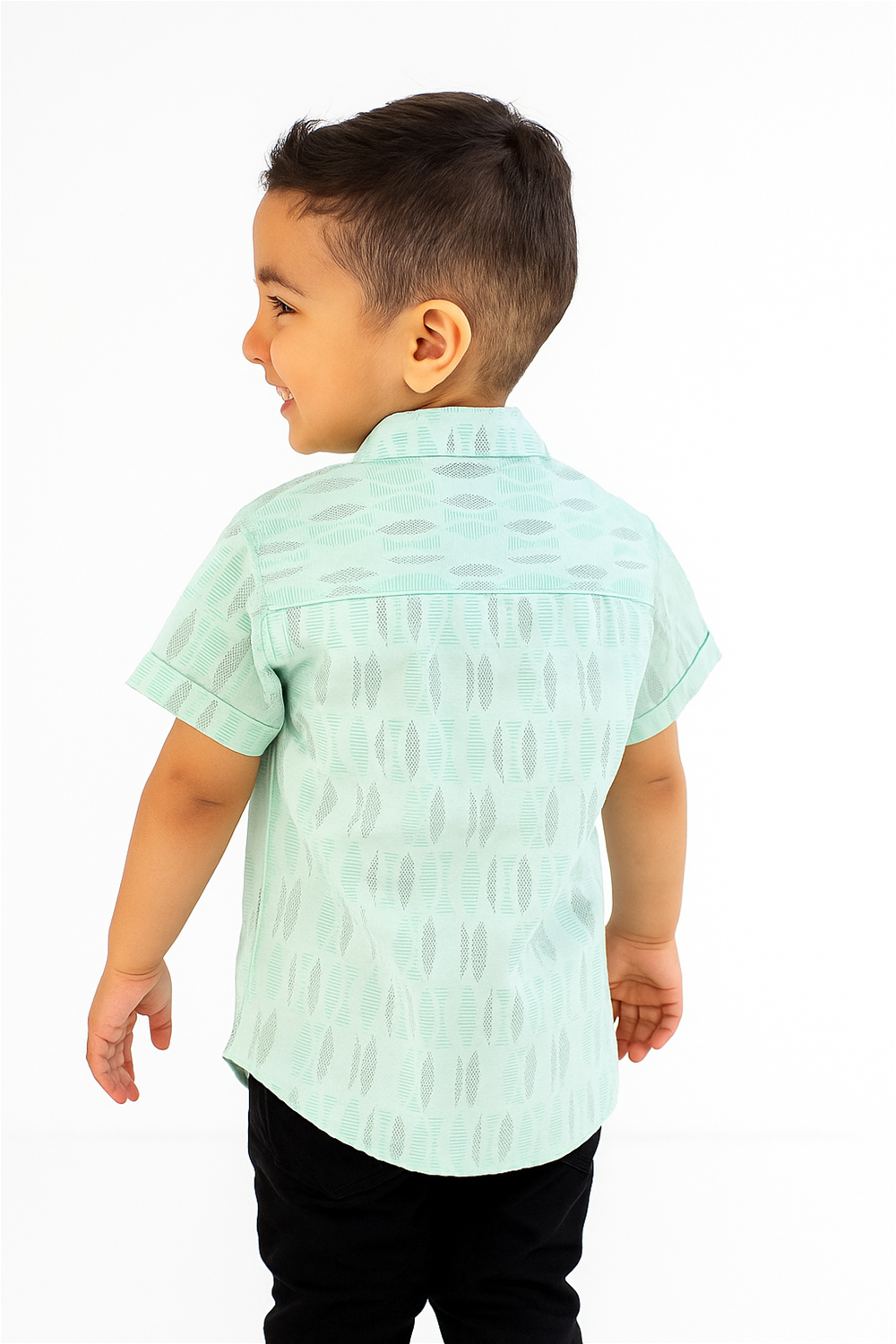 A young boy is seen from the back wearing a mint green half-sleeve Chinese collar shirt with subtle geometric woven patterns. The shirt features a straight back yoke and curved hem, paired with black pants for a clean, modern look.