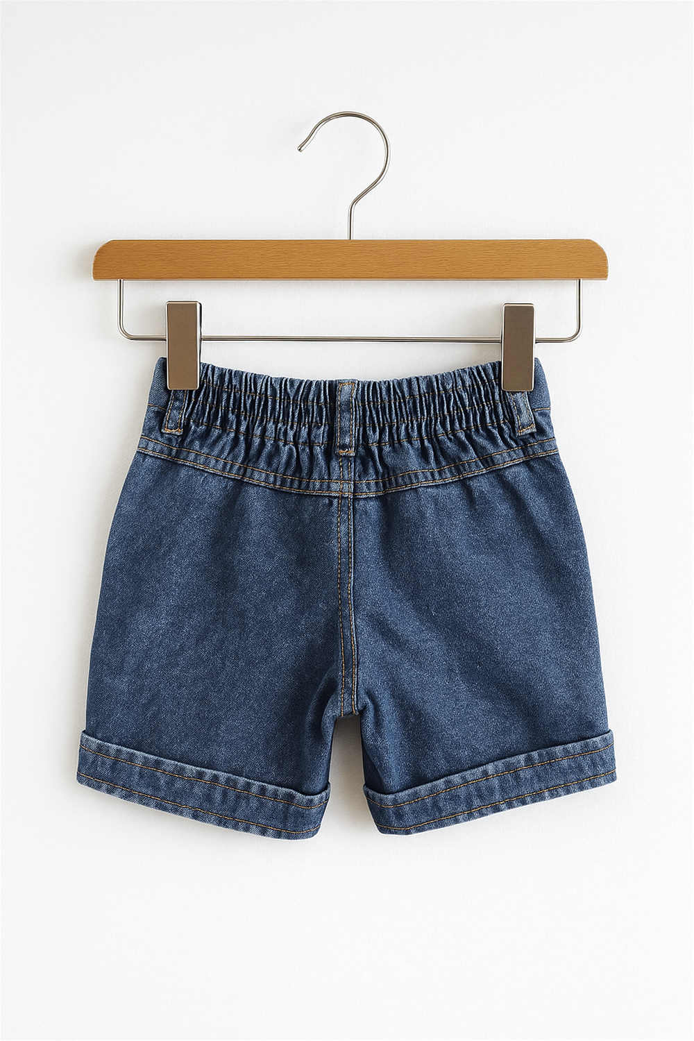 Back view of blue denim shorts on wooden hanger, featuring elastic waistband, double-stitched seams, and rolled hems for durability.