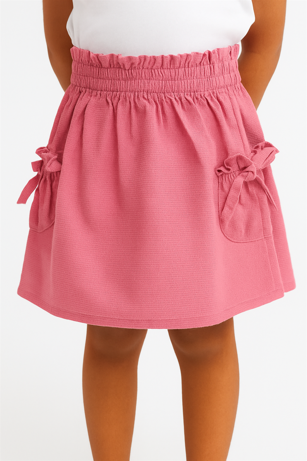 Close-up view of a pink textured skirt with gathered waistband and bow-tied pockets, worn by a child model.
