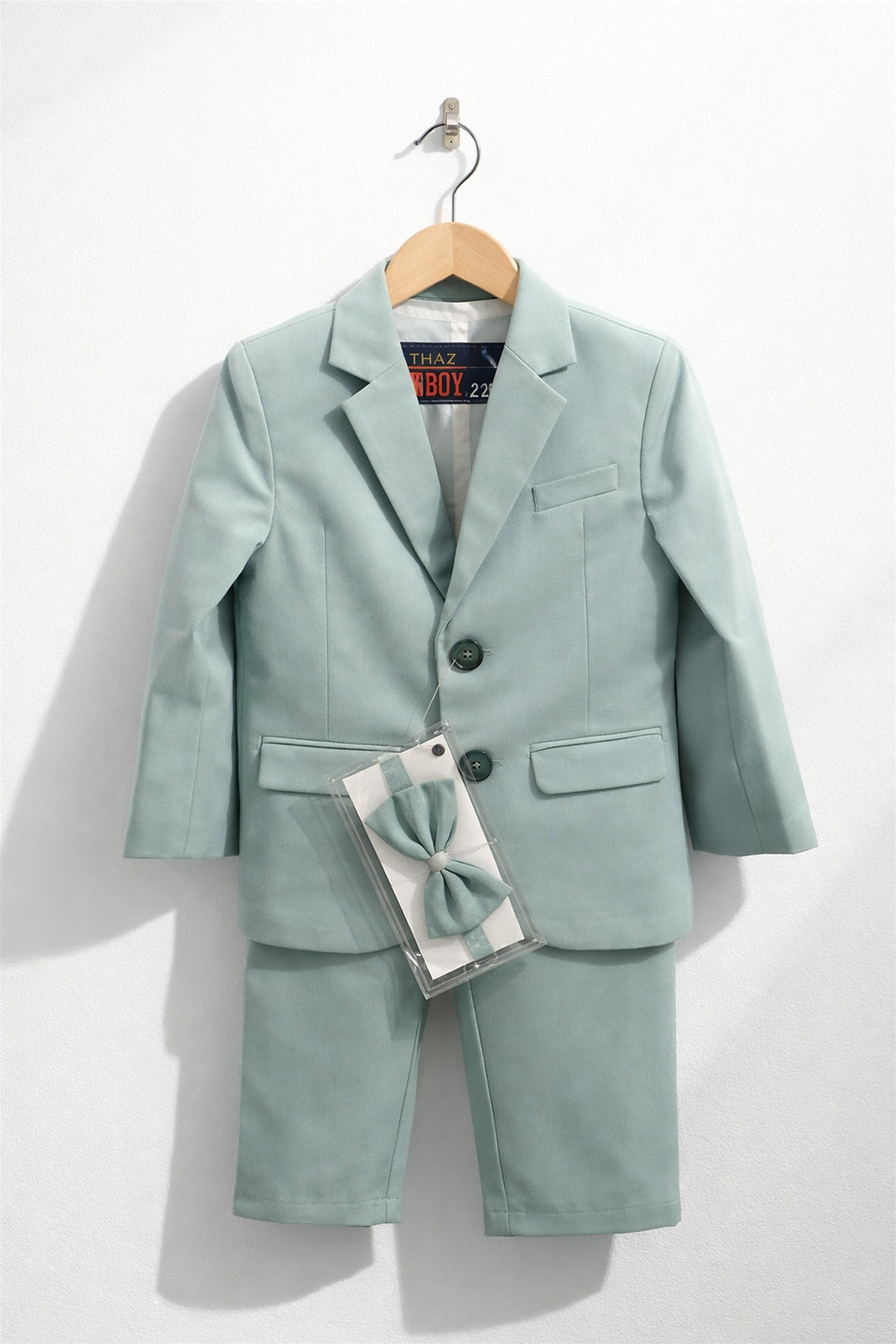 Mint green toddler boy suit displayed on wooden hanger, featuring blazer, trousers, and matching bow tie against clean white background.