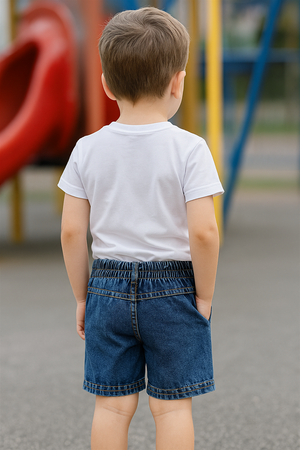 Toddler in white t-shirt and denim shorts, photographed from behind at playground, showing elastic waistband and casual outdoor style.