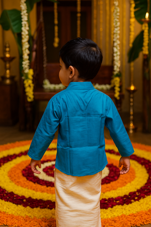 A young boy wearing a bright blue kurta and cream mundu stands with his back to the camera, facing an Onam pookalam made of colorful flower petals. Festive decorations and a wooden swing adorned with garlands create a warm, traditional backdrop.
