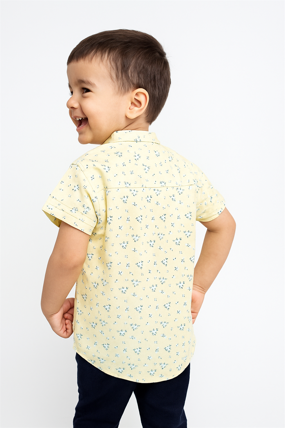 Back view of a young boy wearing a half-sleeve Chinese collar shirt with a light yellow base and delicate floral prints. The shirt offers a comfortable and neat fit, perfect for casual outings or playtime wear.
