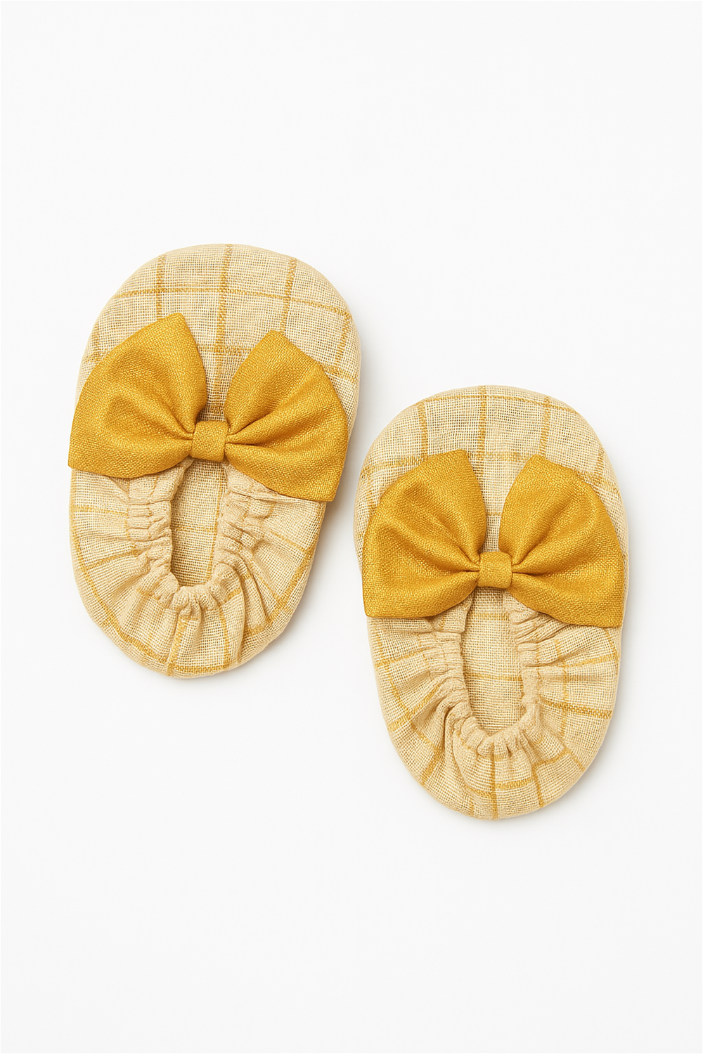 A pair of soft baby booties in beige with golden checks, decorated with large golden bows on the front. The fabric has a gentle texture, and the elastic around the opening ensures a snug and comfortable fit.