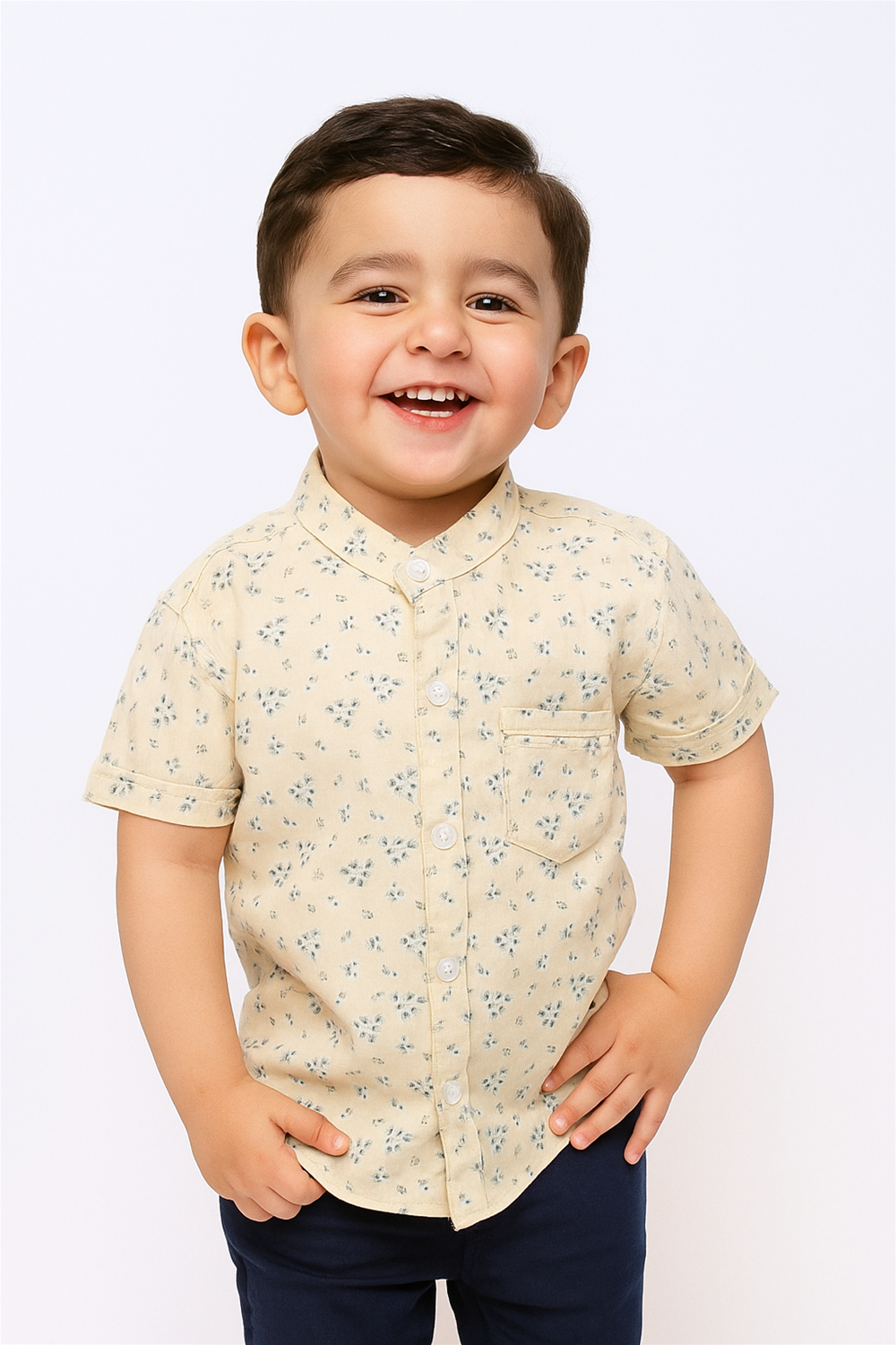 A cheerful young boy wearing a half-sleeve Chinese collar shirt with a light floral print, styled with dark pants. The shirt features a front pocket and button-down design, offering a fresh and smart casual look for kids.