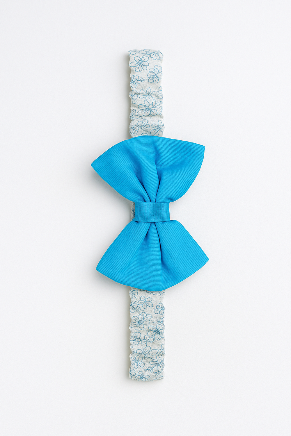 Blue bow headband displayed flat on white background, elastic floral strap with textured bow centered, clean minimal product presentation.