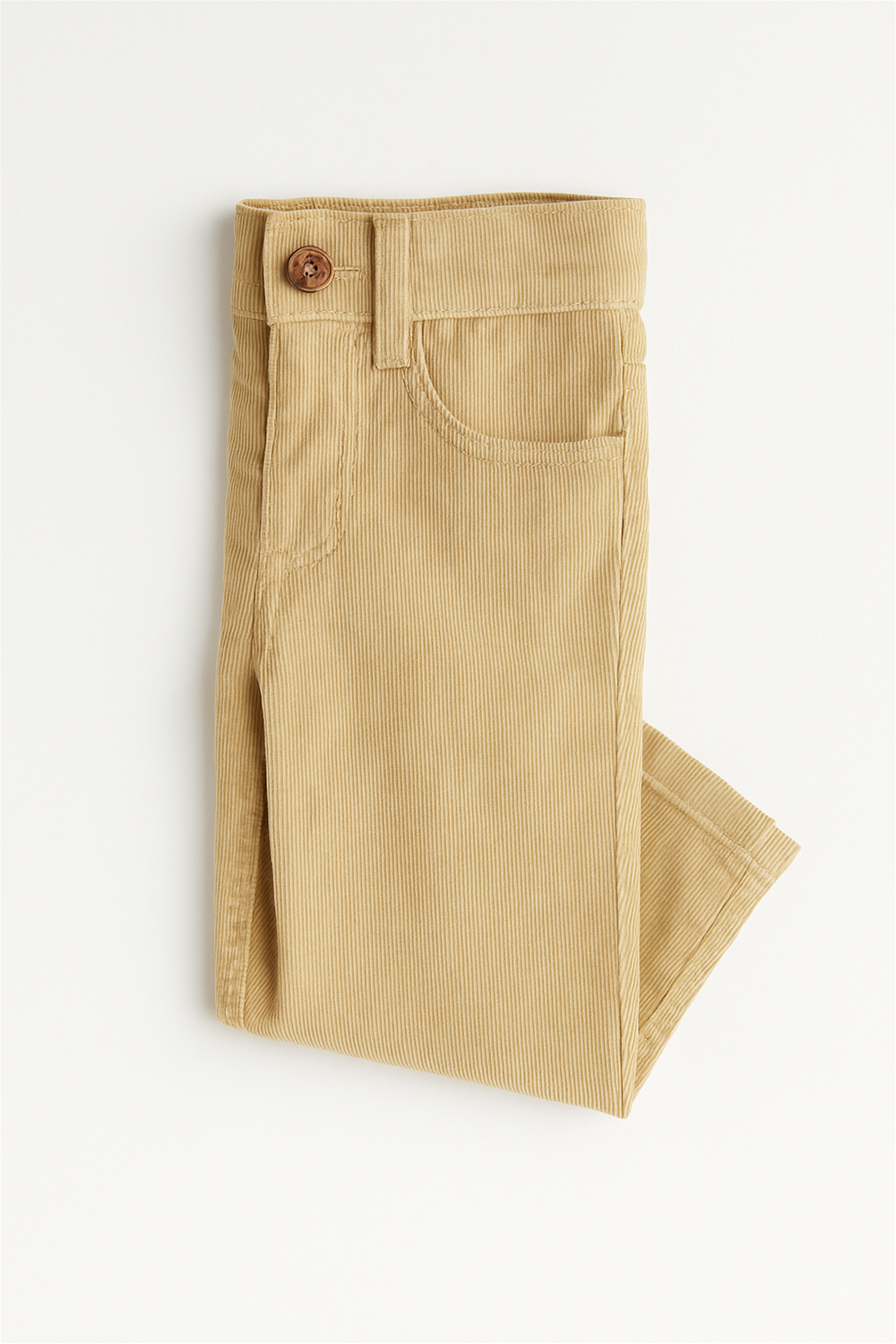 Folded beige corduroy toddler pants displayed on a white background. The pants feature a front scoop pocket, a small coin pocket, belt loops, and a round wooden button closure at the waistband. The fine ribbed fabric provides a soft texture, ideal for comfortable and stylish everyday wear.