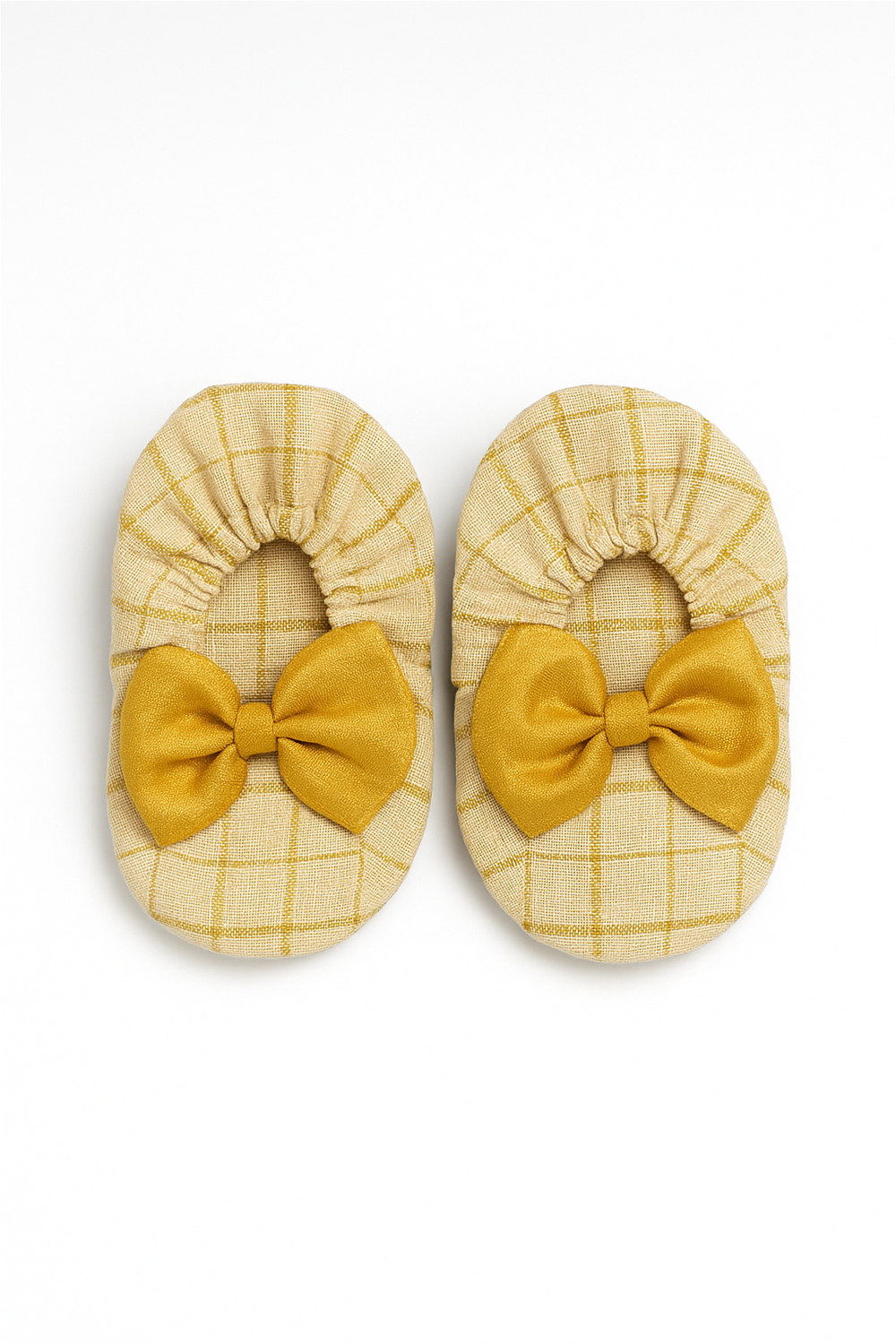 A pair of soft baby booties in beige with golden checks, decorated with large golden bows on the front. The fabric has a gentle texture, and the elastic around the opening ensures a snug and comfortable fit.