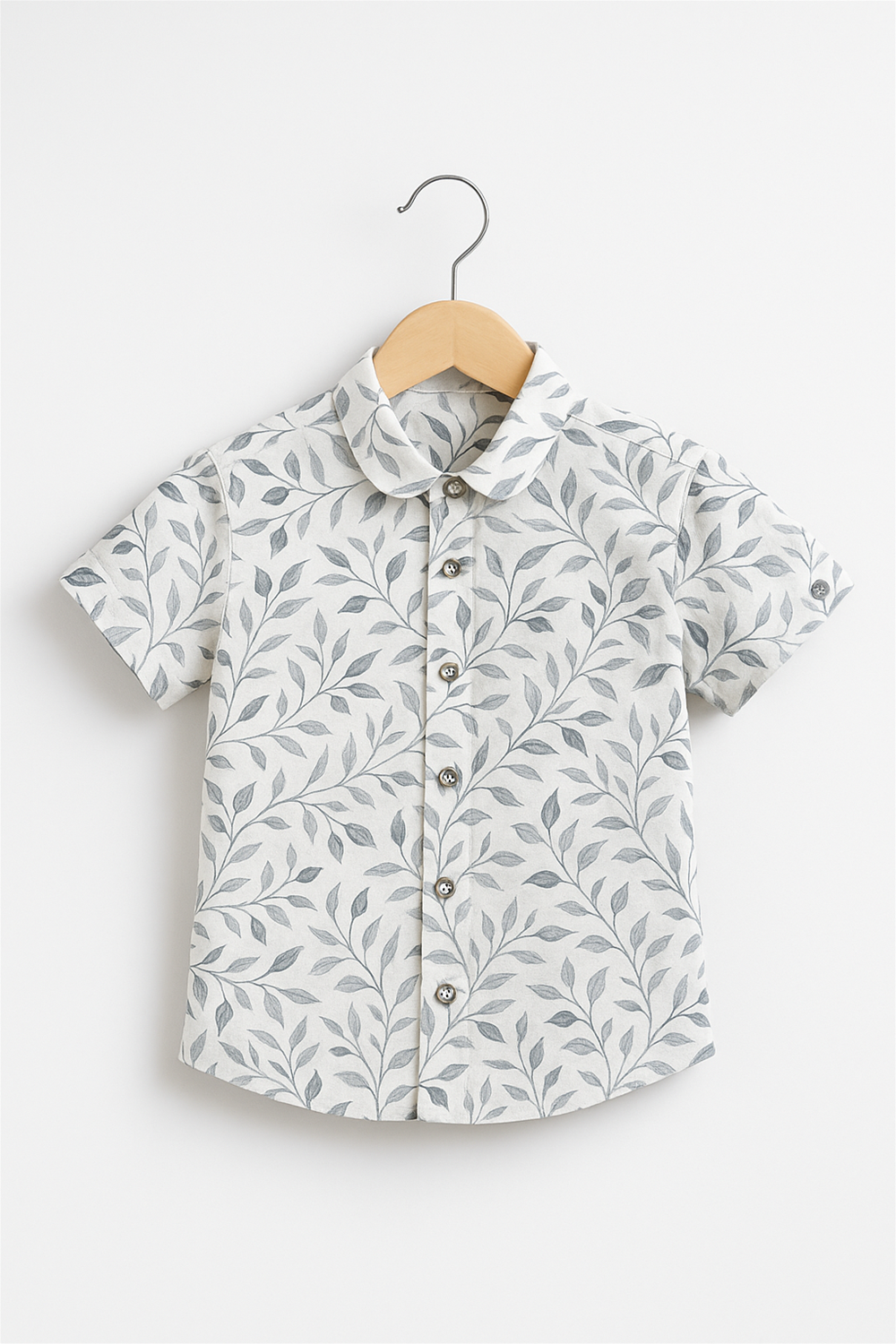 A boy's half-sleeve club collar shirt with a soft off-white base and elegant leafy print. Displayed on a wooden hanger against a clean white background, perfect for catalog or product listings.