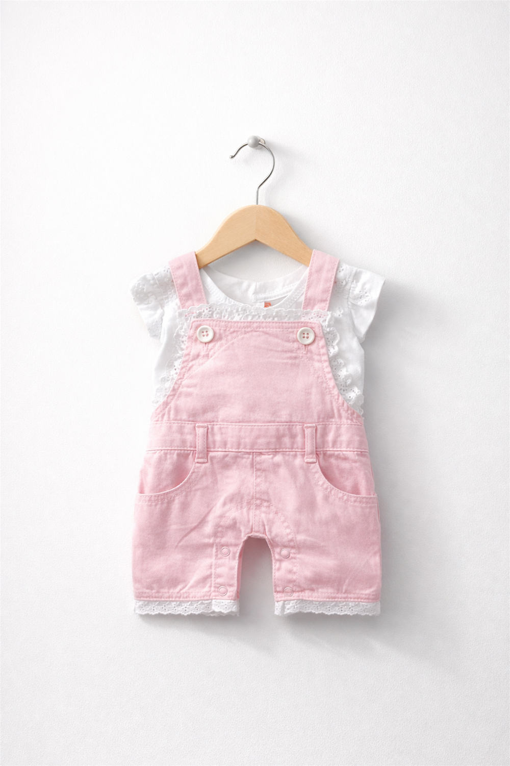 Pink baby dungaree with white inner top, lace-trim hem, neatly displayed on wooden hanger
