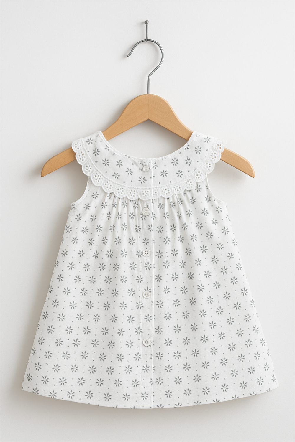 White baby frock with floral lace collar and button-down back, displayed on wooden hanger against clean white studio wall.