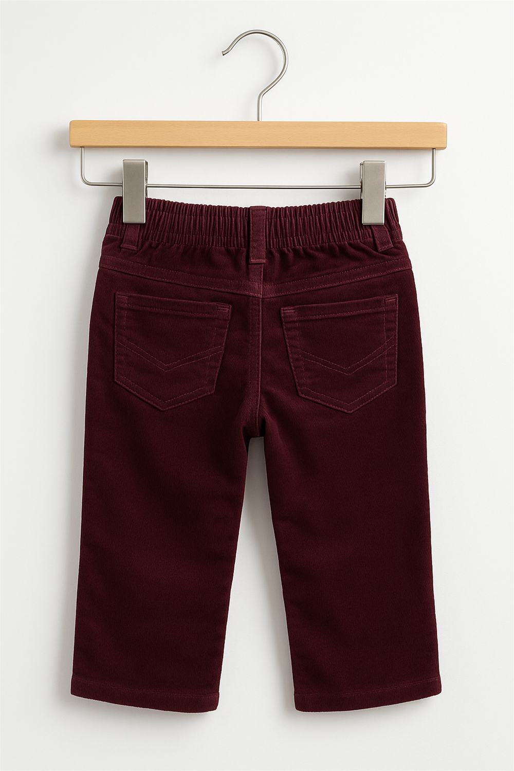 Maroon corduroy boys' full-length pants displayed on a wooden hanger against a white background. The pants feature front scoop pockets, a coin pocket, a waistband with belt loops, and a brown button closure at the center. The design is simple, classic, and neatly presented for product showcasing.
