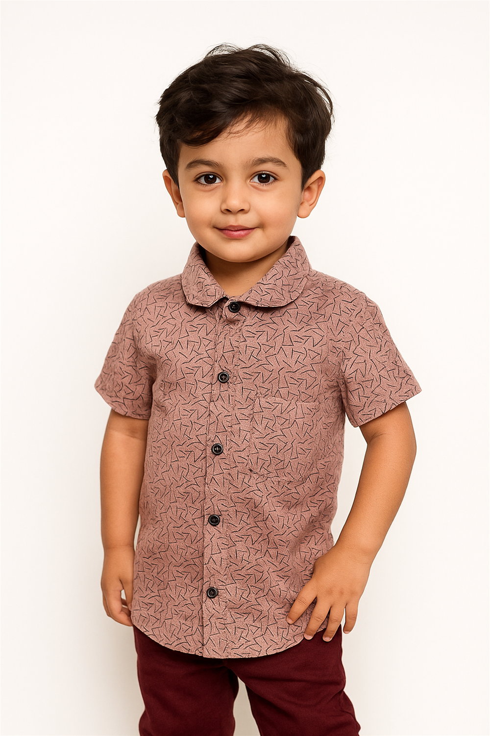A young child wearing a short-sleeved, patterned shirt stands against a plain white background, hands at their sides.