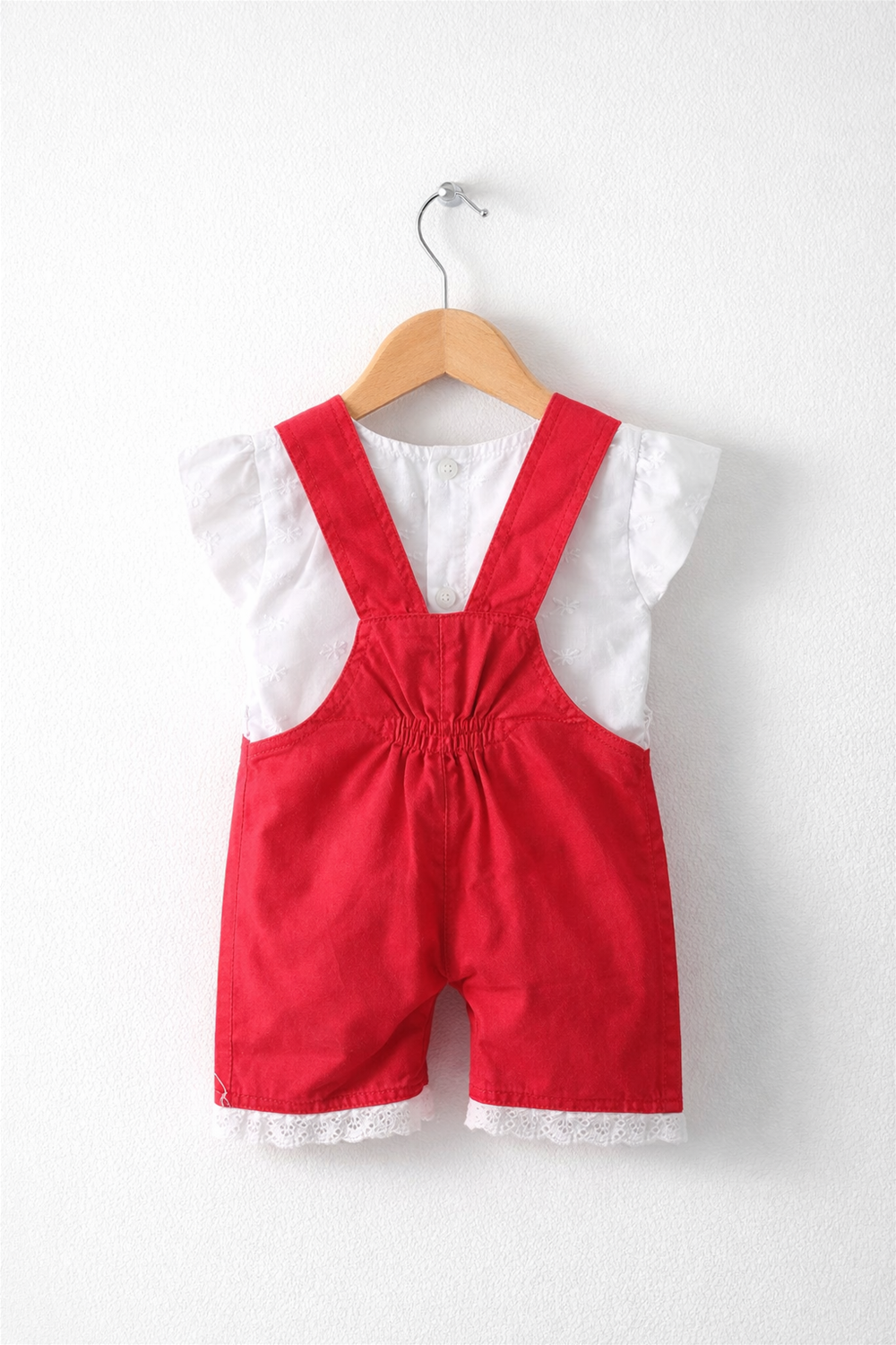 Red baby dungaree with white inner top, elasticated back waist, lace-trim hem, neatly displayed on wooden hanger.