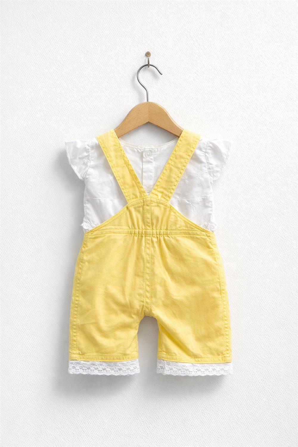 Yellow baby dungaree with white inner top, elasticated back waist, lace-trim hem, neatly displayed on wooden hanger