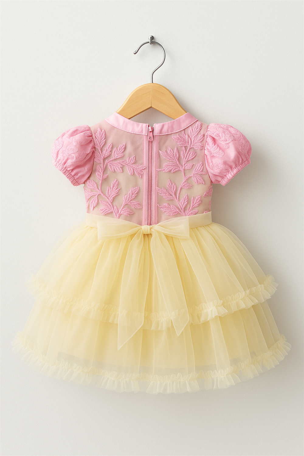A yellow and pink dress in a wooden hanger back view.