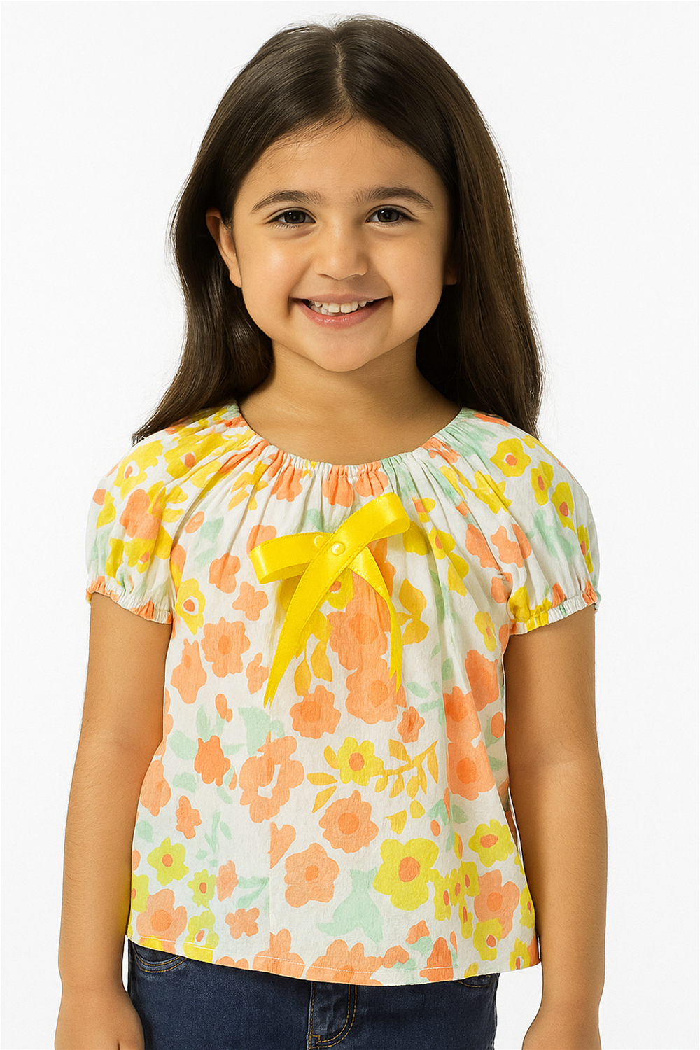 Smiling little girl wearing a floral top with yellow bow detail, puff sleeves, styled with jeans, playful cheerful fashion.