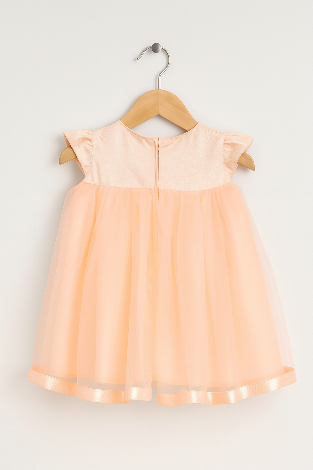 Peach-colored children's dress with cap sleeves and a tulle skirt, hanging on a wooden hanger against a white background.