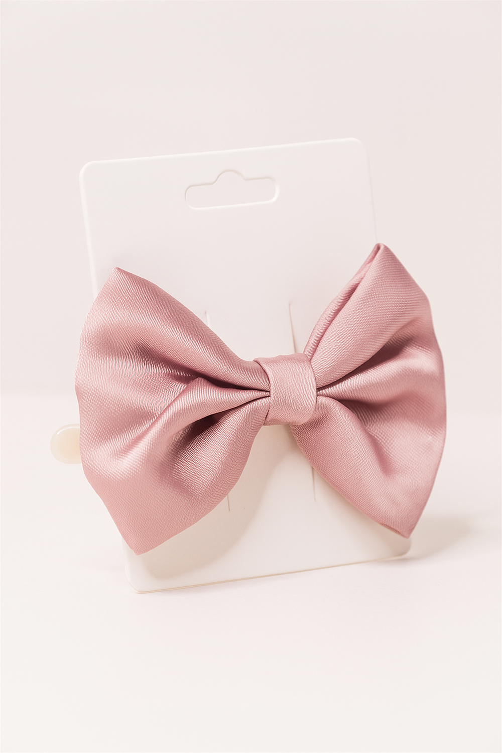 A soft pink satin bow hair clip displayed on a white card, highlighting its smooth fabric texture and elegant shape.