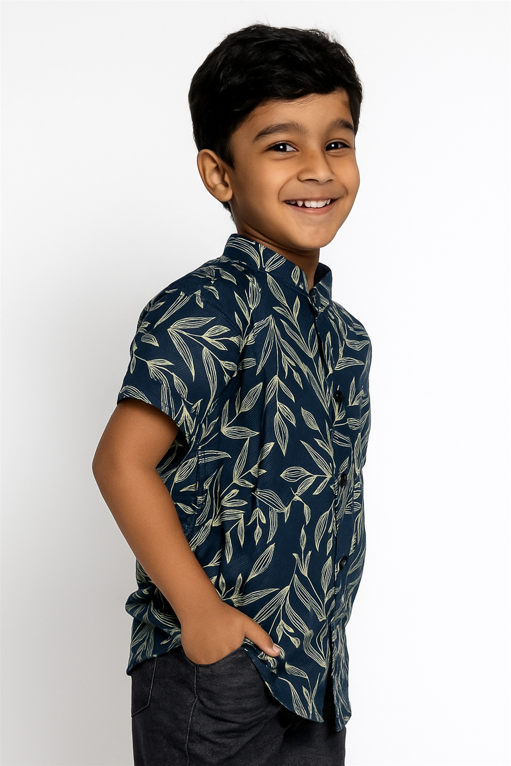 A young boy in a patterned half-sleeve shirt with a Chinese collar, smiling and standing against a neutral background.