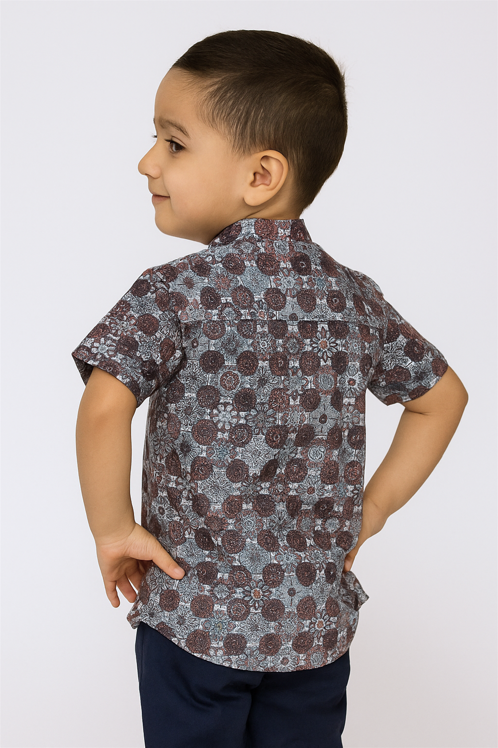 Back view of a toddler boy wearing a half-sleeve Chinese collar shirt with an intricate geometric floral print in earthy tones. The shirt features a straight yoke and tailored finish, offering a smart casual look perfect for any outing.