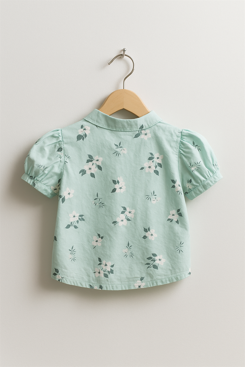 Back view of mint green floral Chinese collar top, puff sleeves and scattered white flower pattern, neatly displayed on wooden hanger.