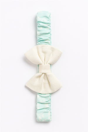 Full view of mint-green elastic hairband with large cream bow centerpiece, styled on a white background for product display.