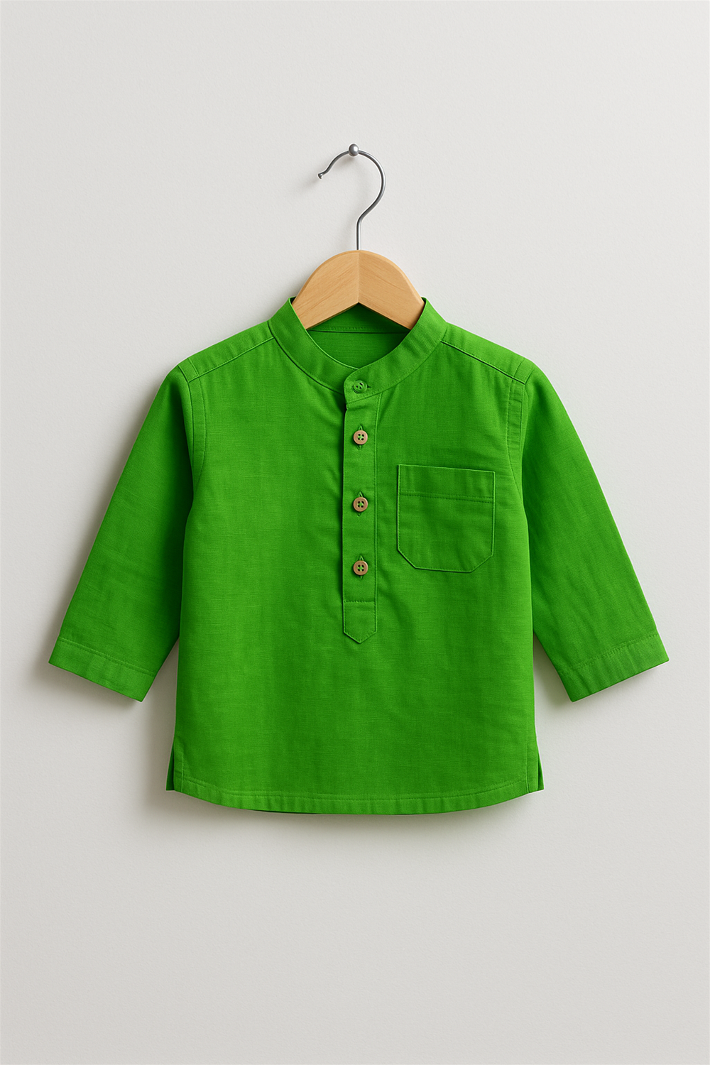 A vibrant green boy’s kurta with a Chinese collar and wooden button placket is displayed on a wooden hanger. The kurta features long sleeves and a single chest pocket, set against a plain white background.