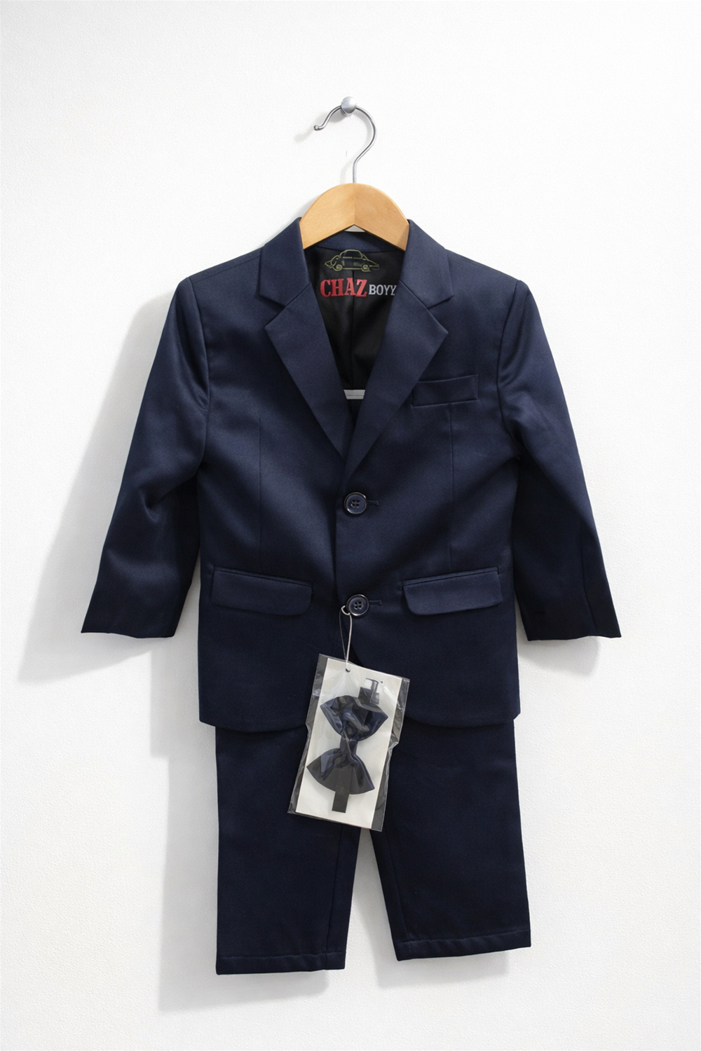 toddler boy suit displayed on wooden hanger, featuring blazer, trousers, and matching bow tie against clean white background.