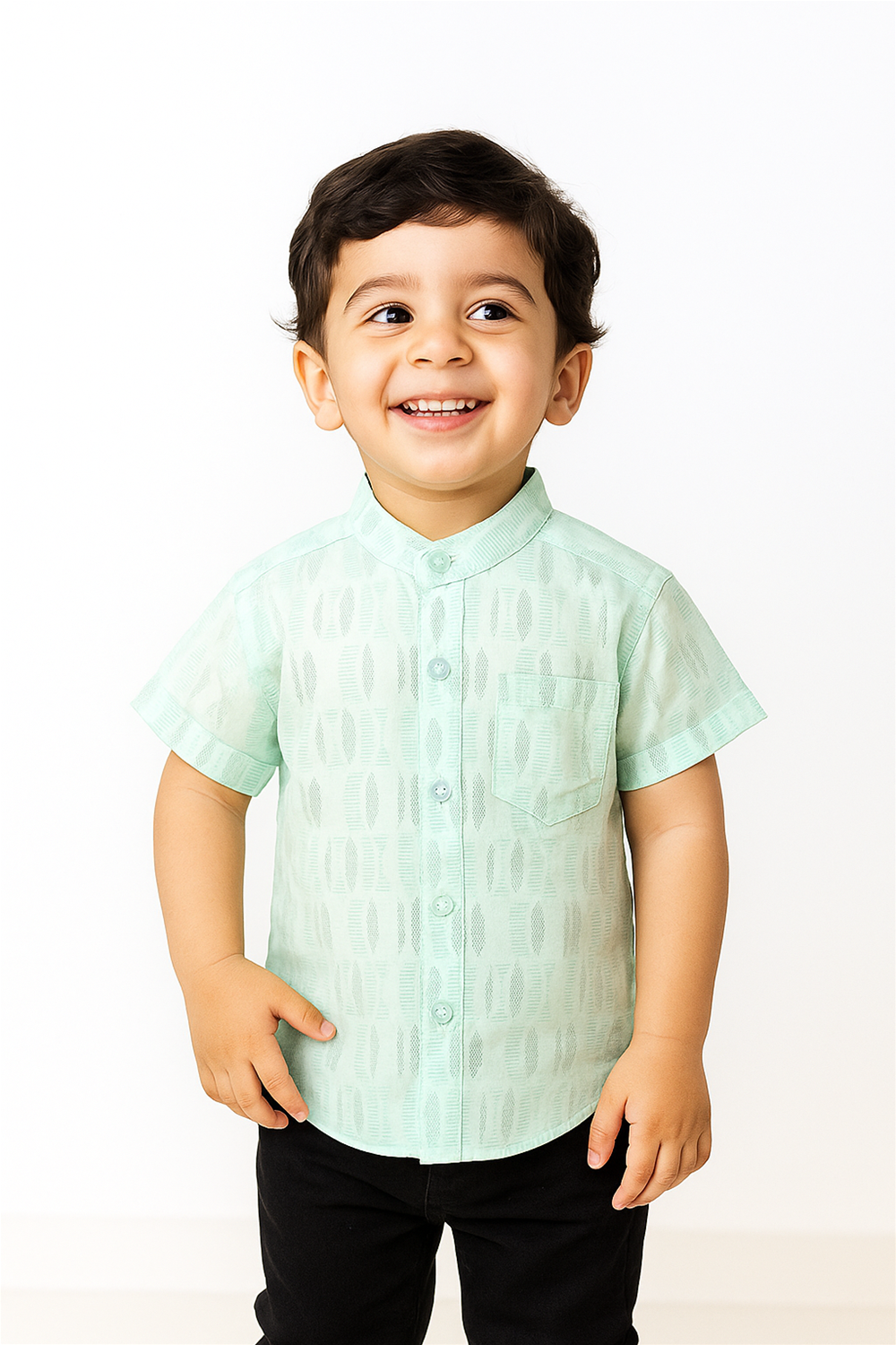 A cheerful young boy wearing a pastel green half-sleeve Chinese collar shirt with textured vertical patterns. The shirt includes a front pocket and button placket, paired with black pants in a bright studio setting.