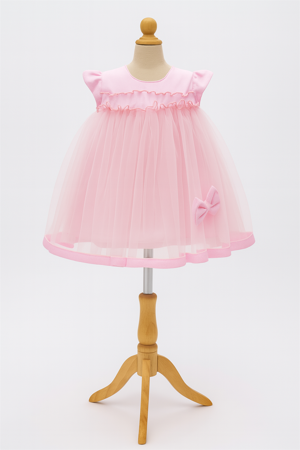 A cute pink toddler dress with a tulle skirt and a bow, displayed on a wooden mannequin against a white background.