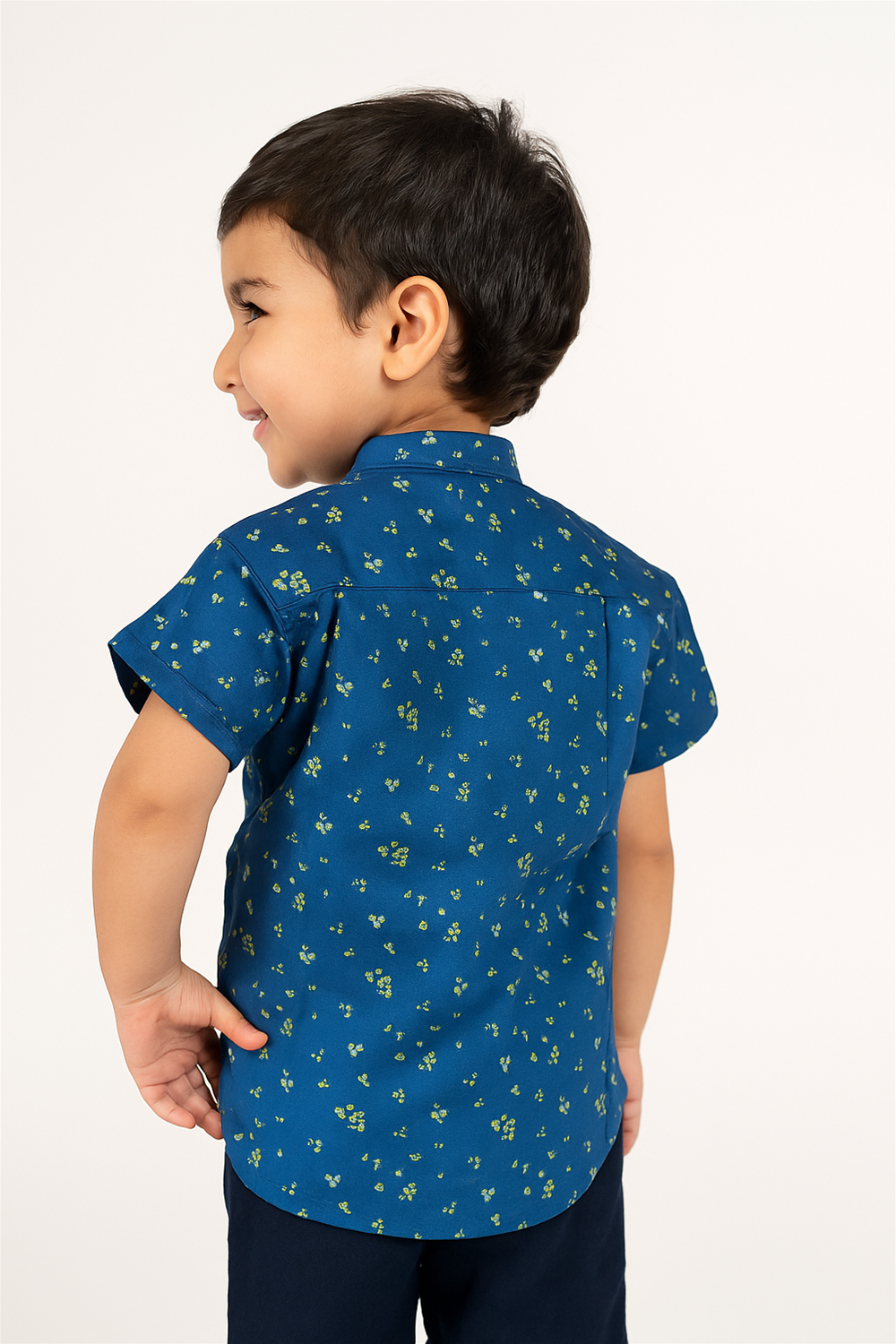 Back view of a toddler boy wearing a half-sleeve Chinese collar shirt in navy blue with tiny green floral prints. The shirt features a yoke detail at the back and is paired with dark navy pants, showcasing a neat and stylish look