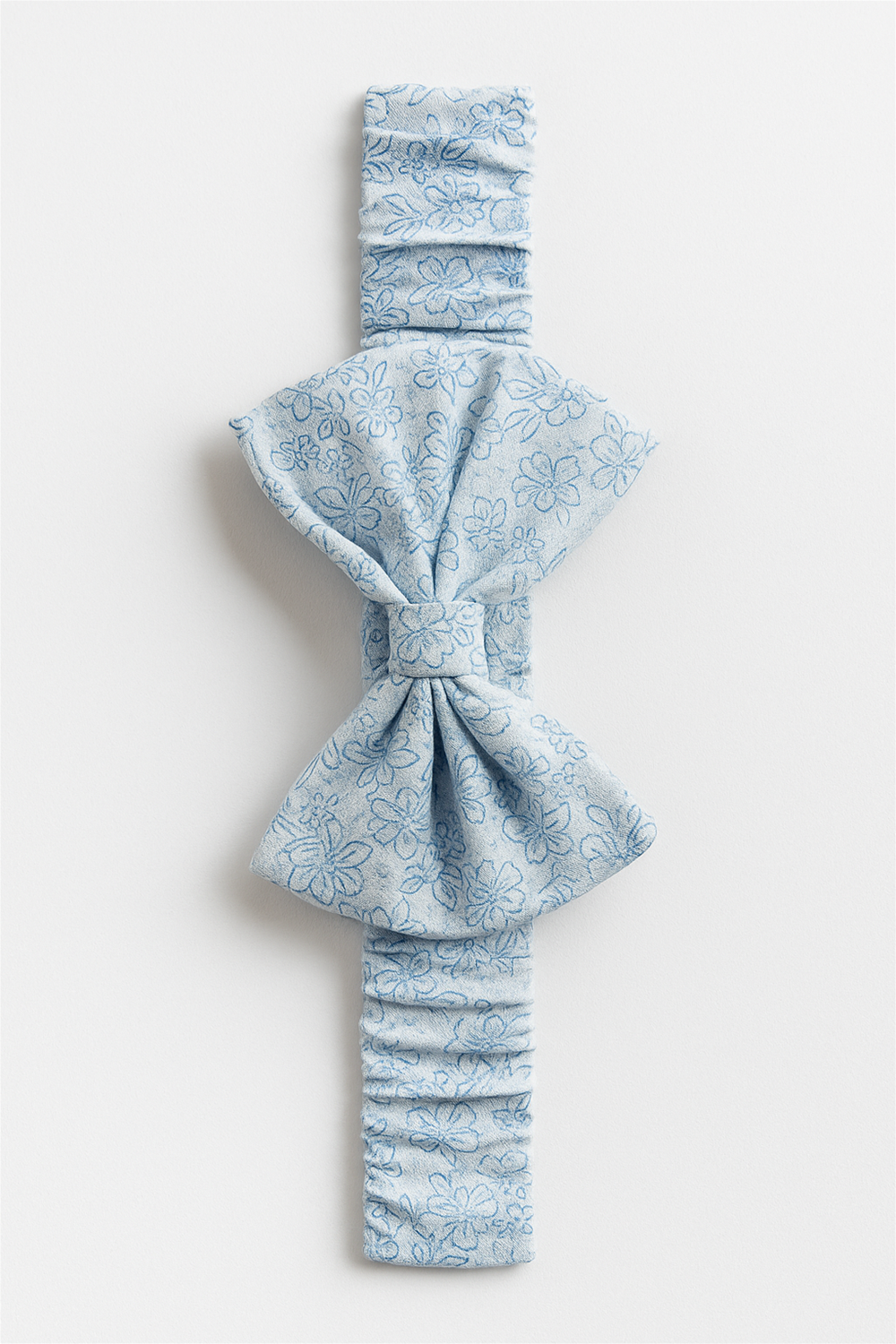 Light blue elastic hairband with a large bow, adorned with delicate floral patterns for a charming look. Designed for babies, it combines comfort with a stylish, soft-textured finish.