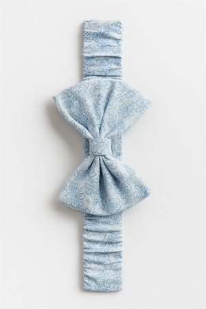 Light blue elastic hairband with a large bow, adorned with delicate floral patterns for a charming look. Designed for babies, it combines comfort with a stylish, soft-textured finish.