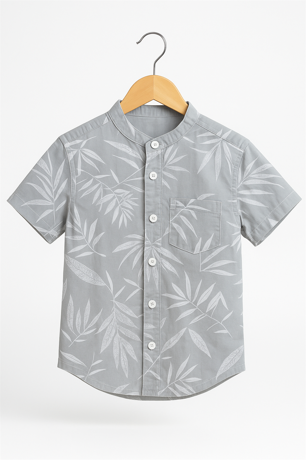 A boys’ half-sleeve shirt with a Chinese collar, displayed on a wooden hanger against a white background. The light grey shirt features a subtle white leaf print and a front pocket with button-down styling.