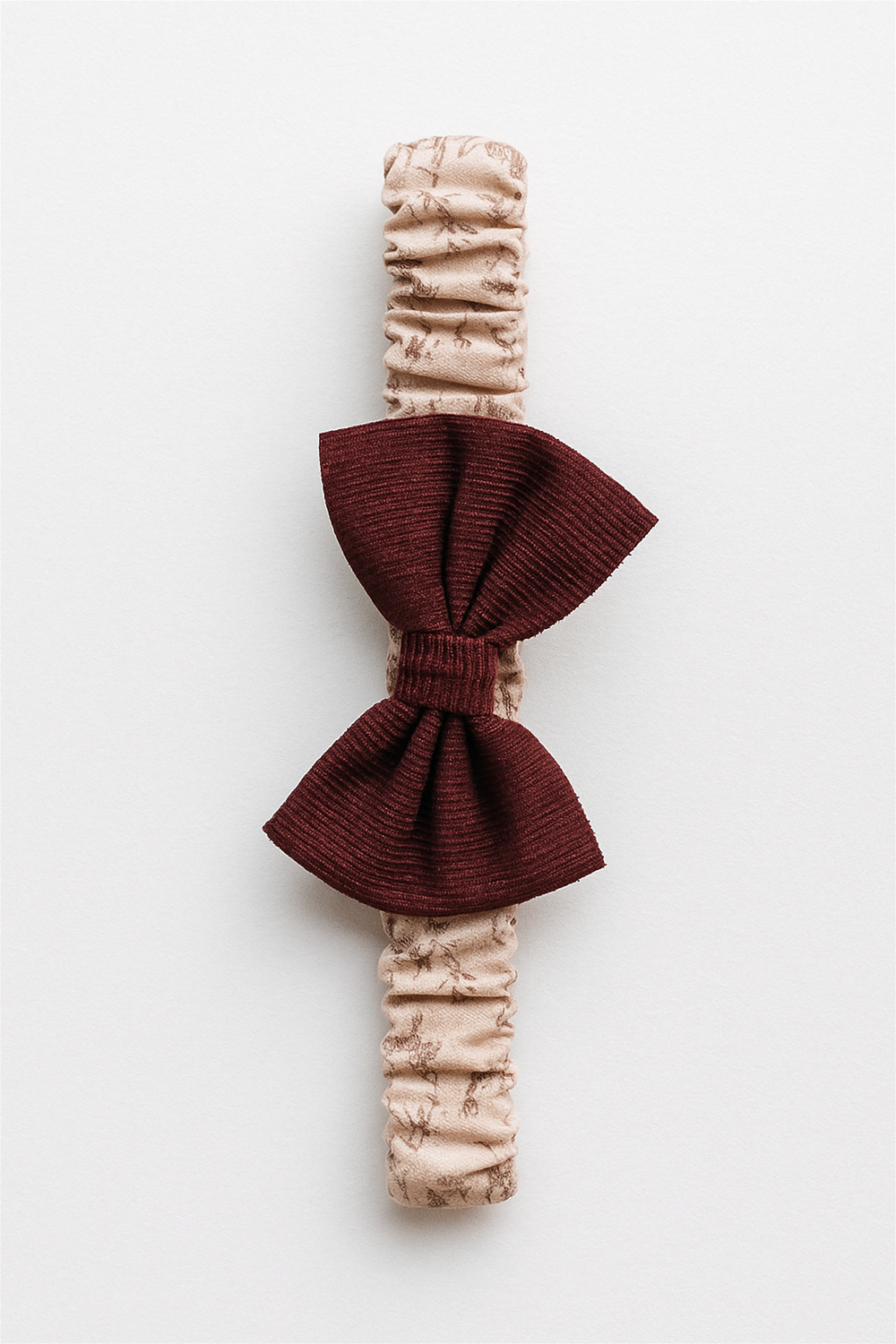 Beige elastic baby headband with burgundy corduroy bow, displayed on a white background in a clean product showcase style.