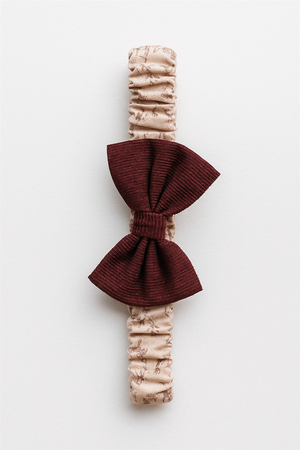 Beige elastic baby headband with burgundy corduroy bow, displayed on a white background in a clean product showcase style.