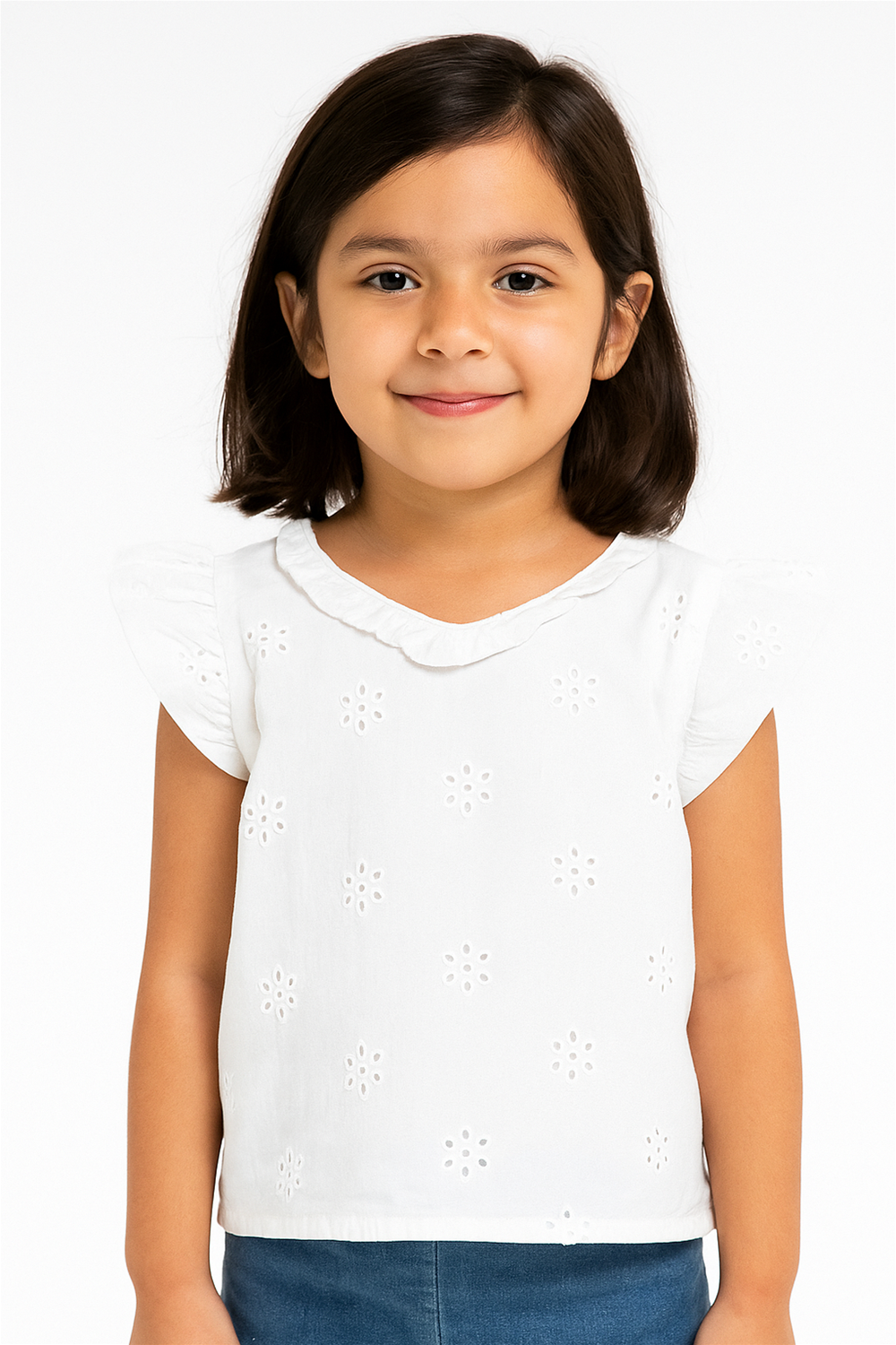 Smiling girl in white embroidered cotton top with flutter sleeves, round ruffled neckline, and delicate floral patterns paired with jeans.