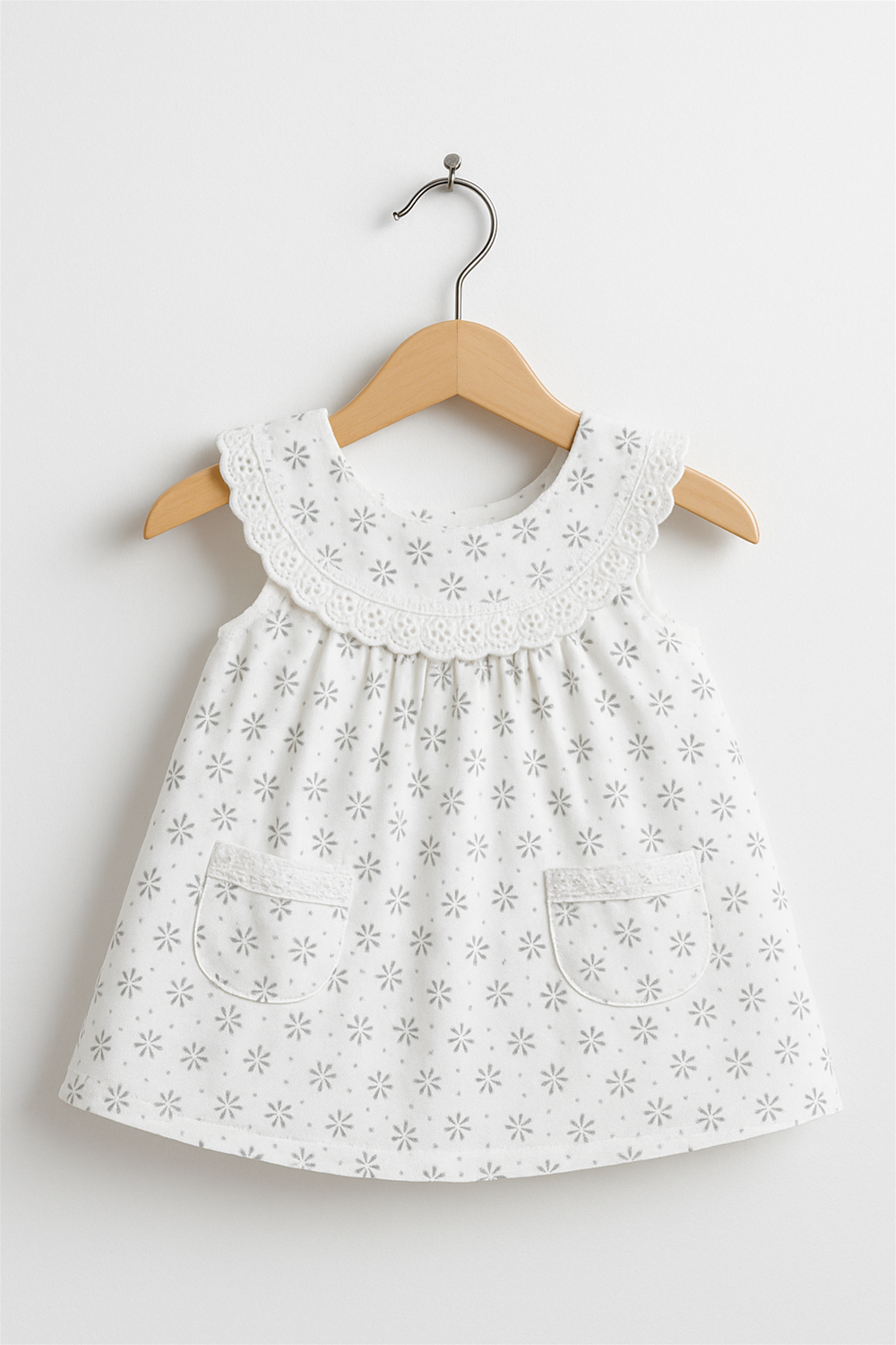 White sleeveless frock with lace collar and twin pockets, floral star embroidery, neatly displayed on wooden hanger for clarity.