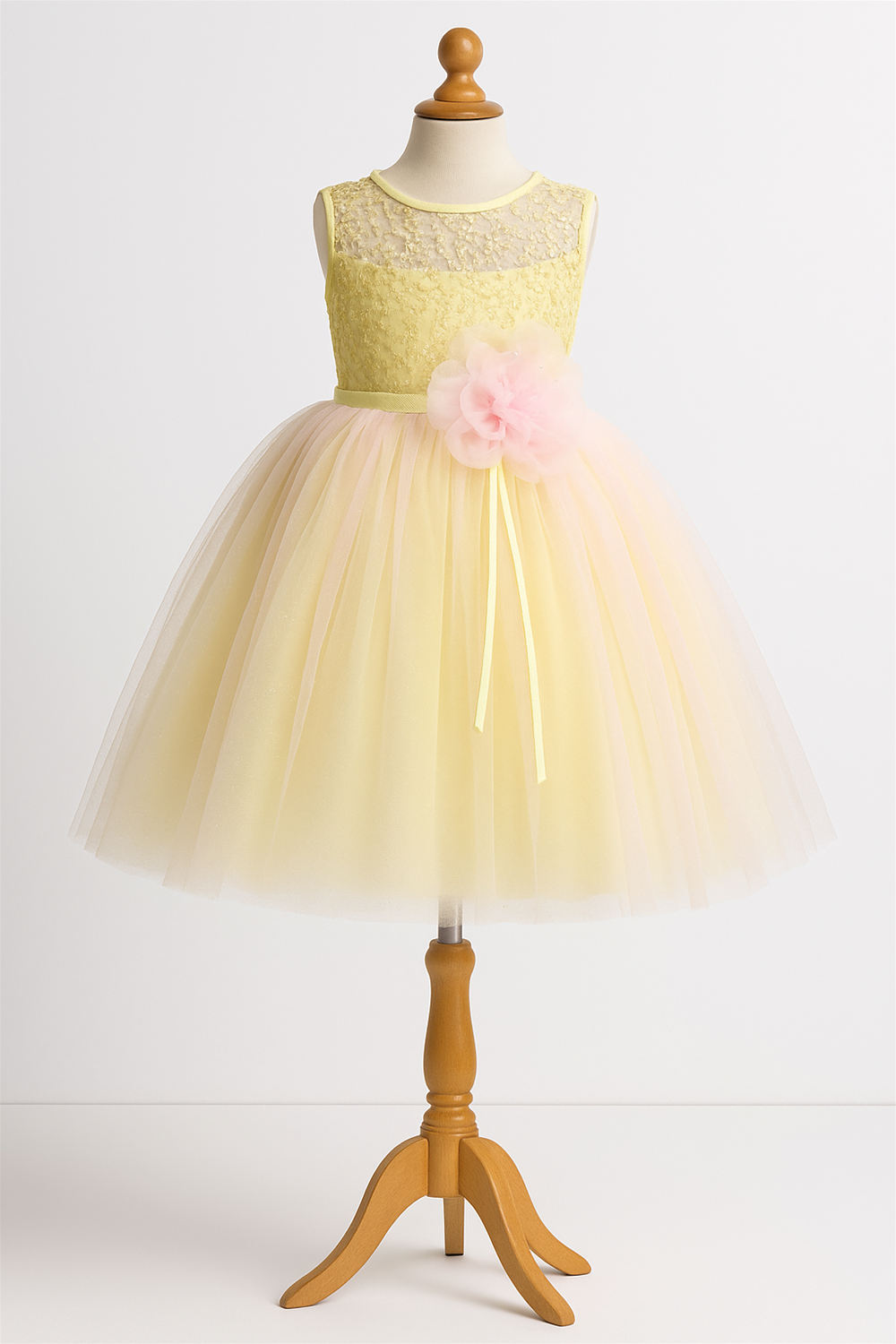 A yellow sleeveless party frock on a mannequin featuring a lace bodice, tulle skirt, and a large pink flower accent.