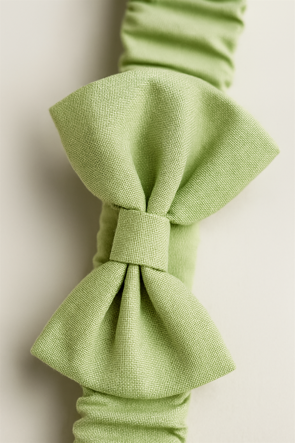 A light green elastic headband featuring a large, neatly tied bow at the center. The headband has a ruched, stretchable band design, providing both comfort and a secure fit.