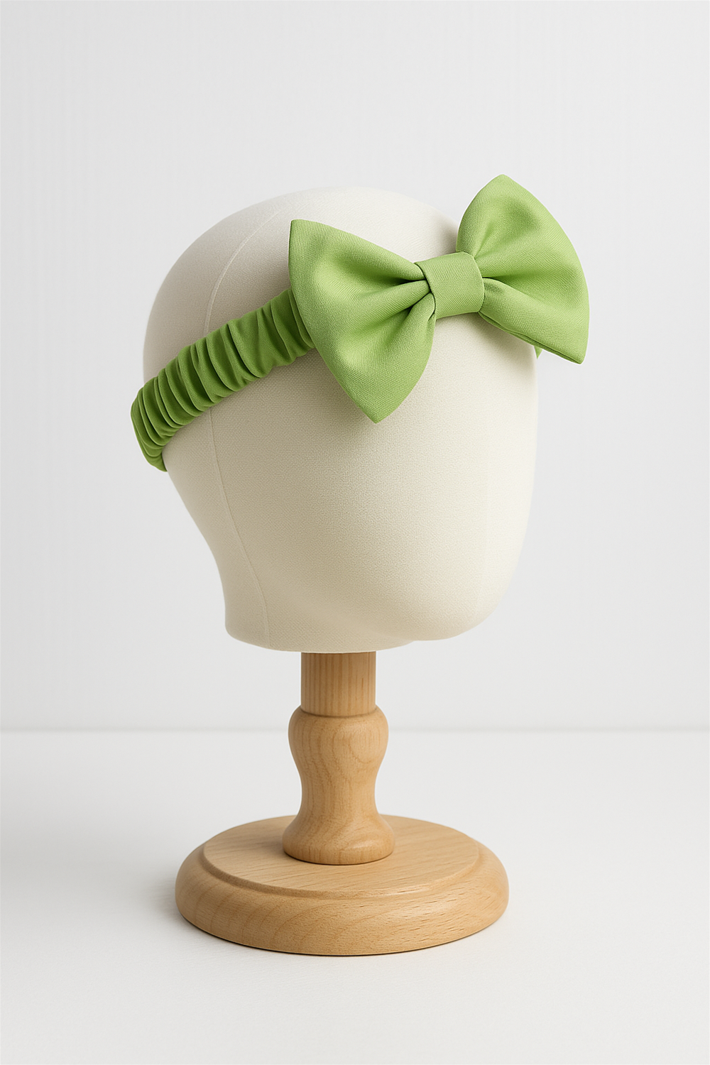 A light green elastic headband featuring a large, neatly tied bow at the center. The headband has a ruched, stretchable band design, providing both comfort and a secure fit.