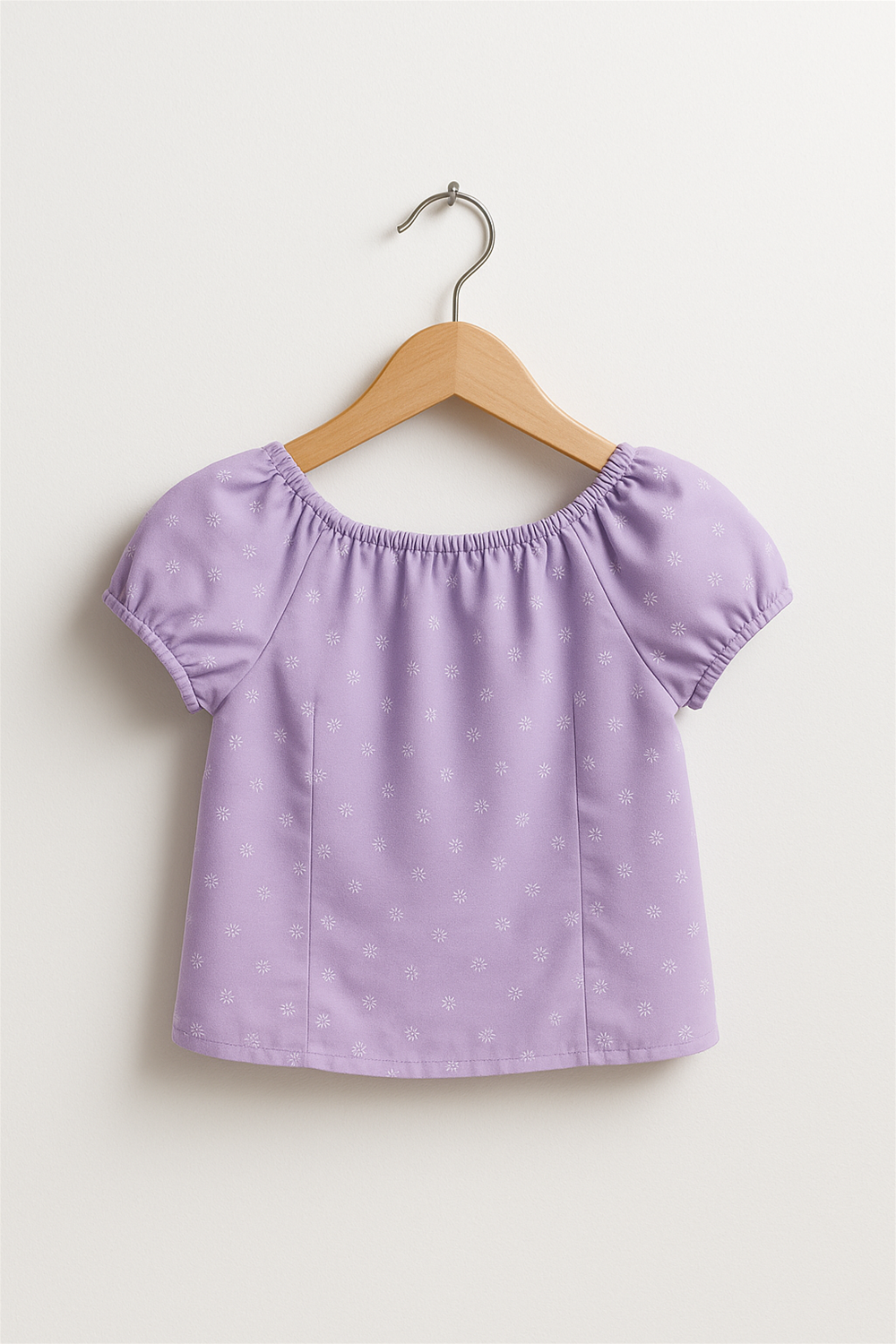 Lavender girls’ top on wooden hanger with elastic neckline and puff sleeves, featuring small white floral embroidery, displayed against plain background.
