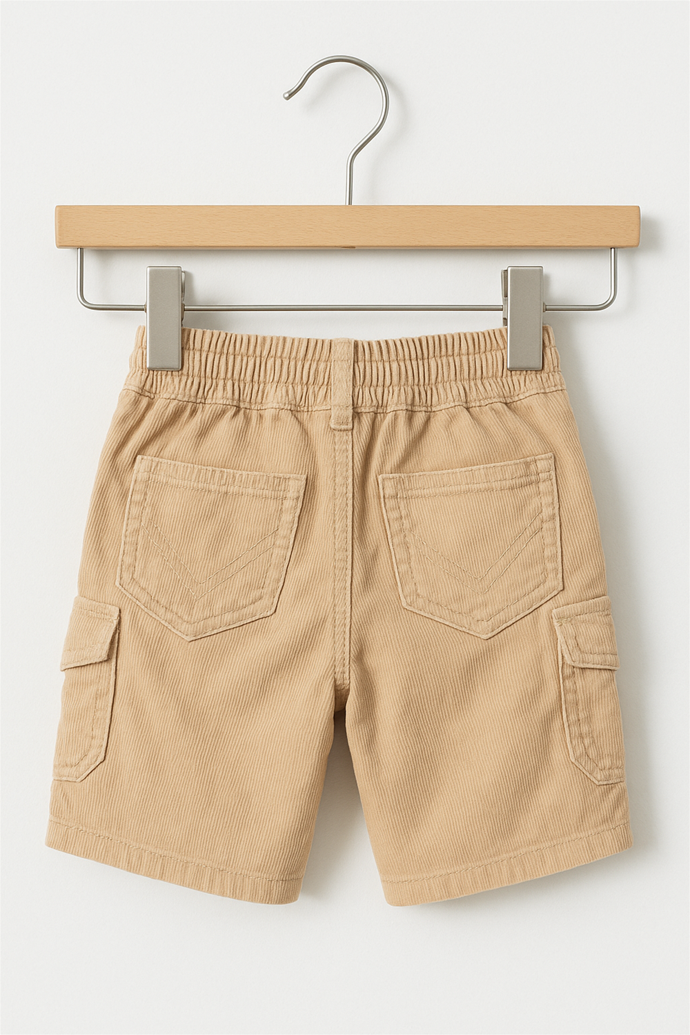 Beige corduroy boys' cargo half pants hanging on a wooden hanger against a white background. The shorts feature front pockets, buttoned flap side pockets, a waistband with belt loops, and a front button closure.