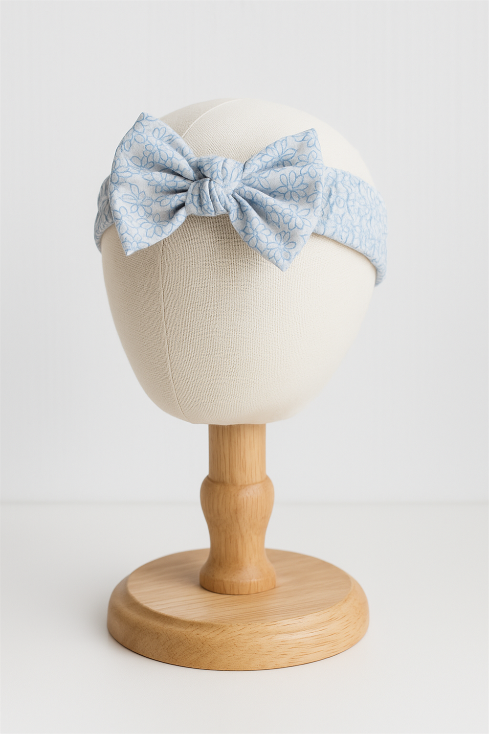In head foam mannequin. Light blue elastic hairband with a large bow, adorned with delicate floral patterns for a charming look. Designed for babies, it combines comfort with a stylish, soft-textured finish.