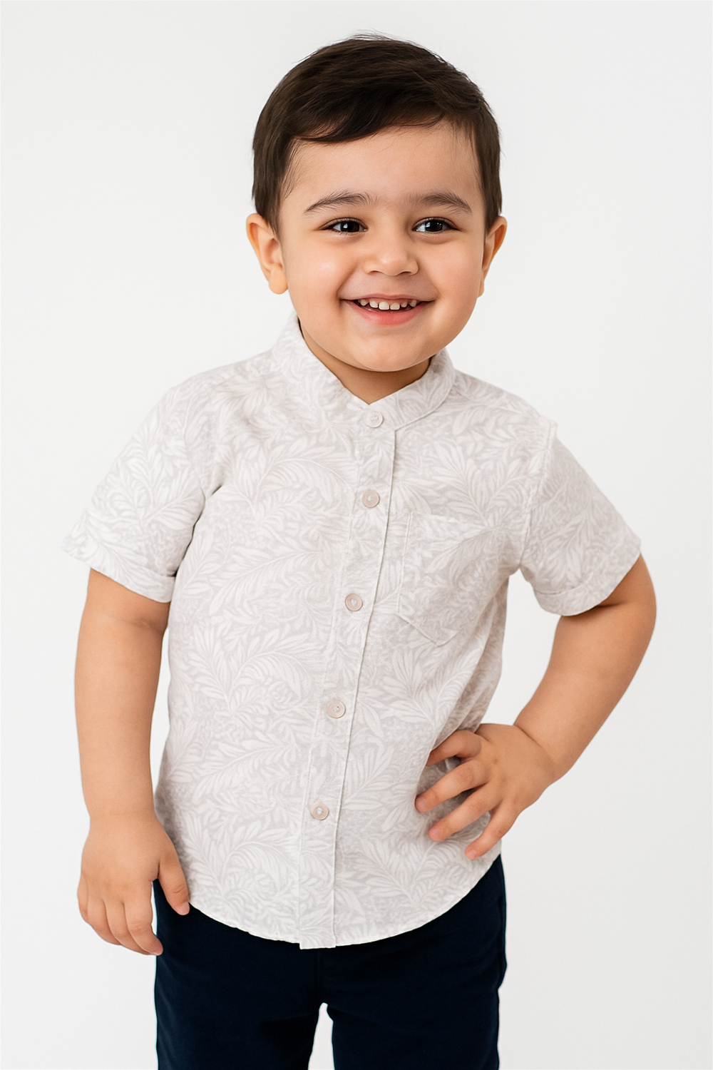 A cheerful young boy wears a half-sleeve Chinese collar shirt in soft beige with subtle leafy patterns. The shirt features a front pocket and tonal buttons, styled in a playful and comfortable fit.