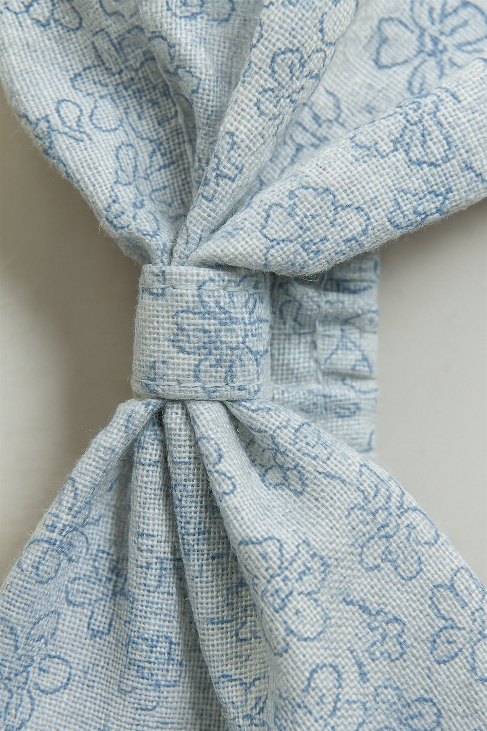 Close up image. Light blue elastic hairband with a large bow, adorned with delicate floral patterns for a charming look. Designed for babies, it combines comfort with a stylish, soft-textured finish.