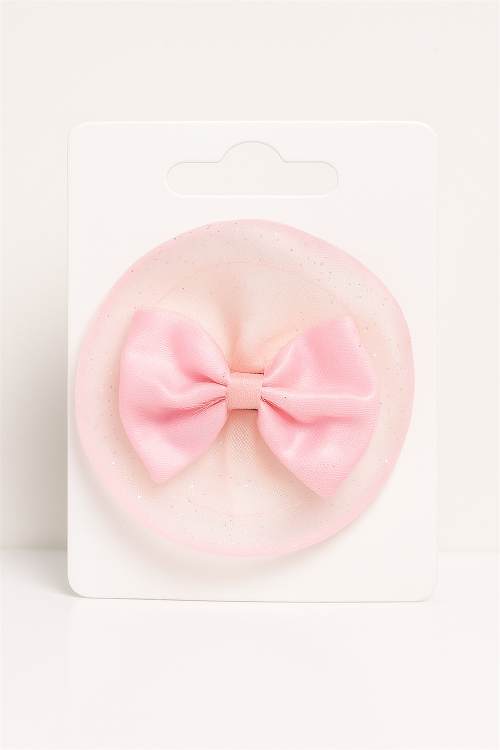 “Pink satin bow hair clip with sheer net base, displayed on a white card against minimal background.”