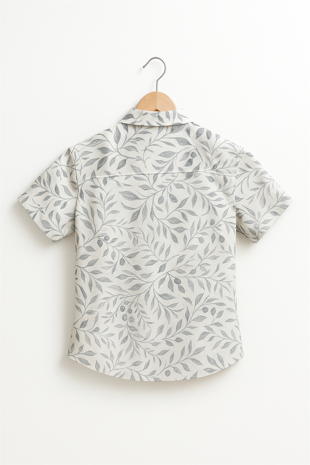 Back view of a boy's half-sleeve club collar shirt with a soft off-white base and elegant leaf print. Displayed on a wooden hanger, highlighting the seamless back design and lightweight summer fabric.